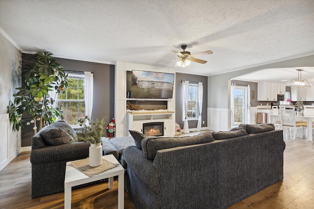 living room with a textured ceiling, ceiling fan, light wood-type flooring, and crown molding