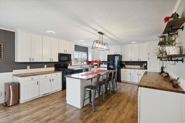 kitchen featuring white cabinets, a kitchen island, butcher block counters, and black appliances