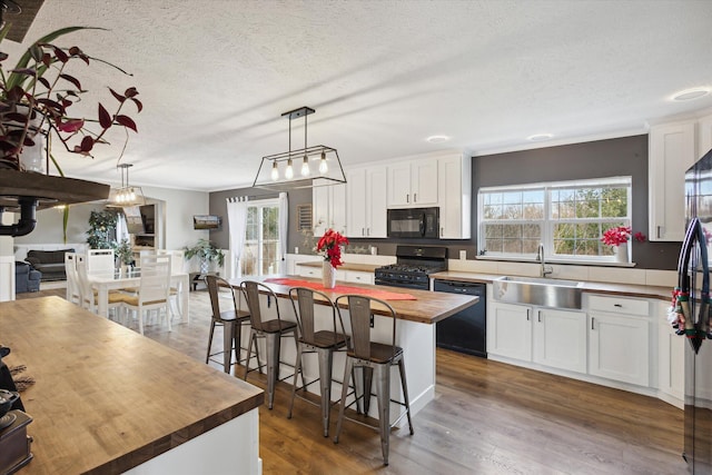 kitchen featuring a kitchen island, butcher block countertops, pendant lighting, white cabinets, and black appliances