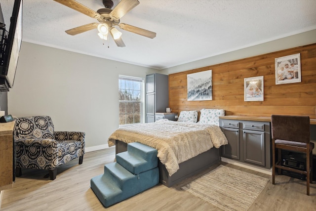 bedroom featuring a textured ceiling, light hardwood / wood-style flooring, ceiling fan, and wood walls