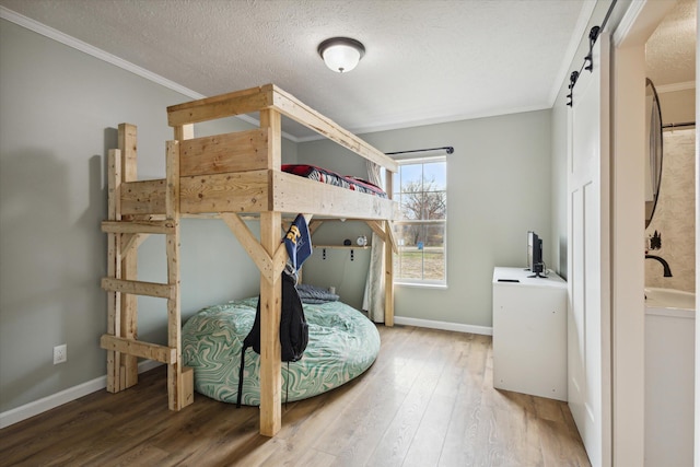 bedroom with a barn door, crown molding, wood-type flooring, and a textured ceiling