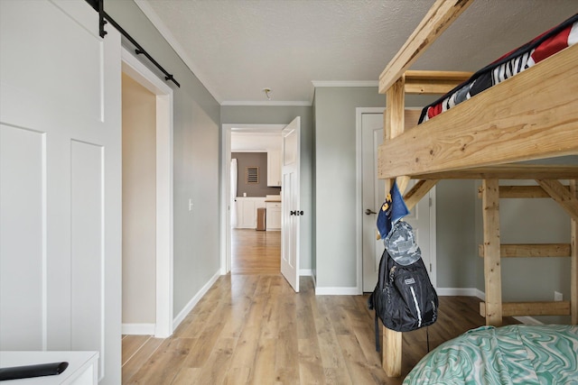 bedroom with a barn door, crown molding, hardwood / wood-style floors, and a textured ceiling