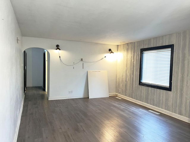 unfurnished room featuring baseboards, visible vents, arched walkways, and dark wood-style flooring