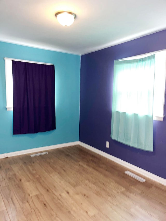 empty room with light wood finished floors, visible vents, and baseboards