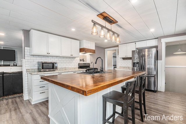 kitchen with wood counters, a kitchen island with sink, sink, and appliances with stainless steel finishes