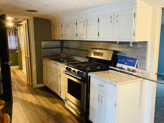 kitchen with sink, stainless steel gas range, a textured ceiling, white cabinets, and light wood-type flooring