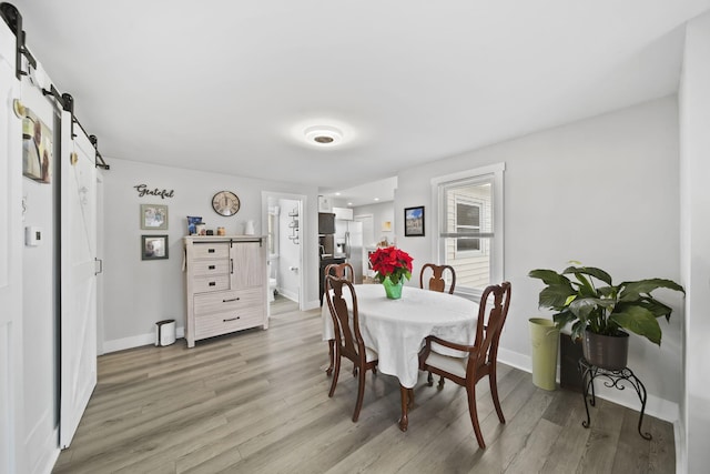 dining space with a barn door and light hardwood / wood-style flooring