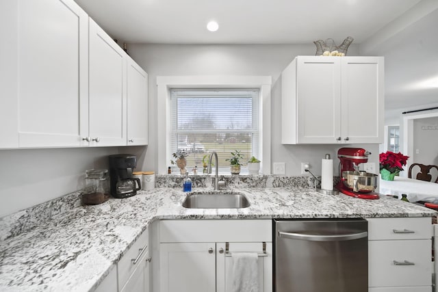 kitchen with light stone counters, white cabinetry, stainless steel dishwasher, and sink