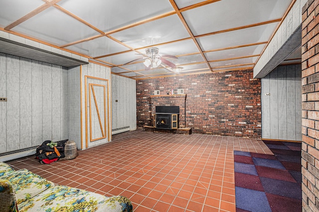 basement featuring wood walls, a wood stove, tile patterned floors, baseboard heating, and brick wall