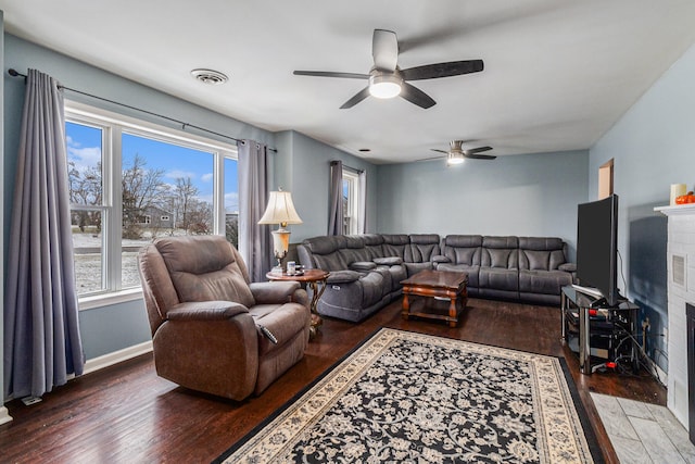 living room with a fireplace, a wealth of natural light, dark wood-type flooring, and ceiling fan