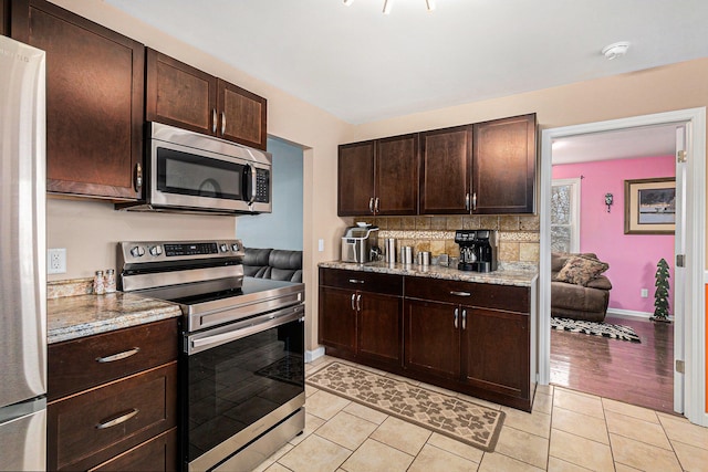 kitchen with dark brown cabinetry, light stone counters, backsplash, light hardwood / wood-style floors, and appliances with stainless steel finishes