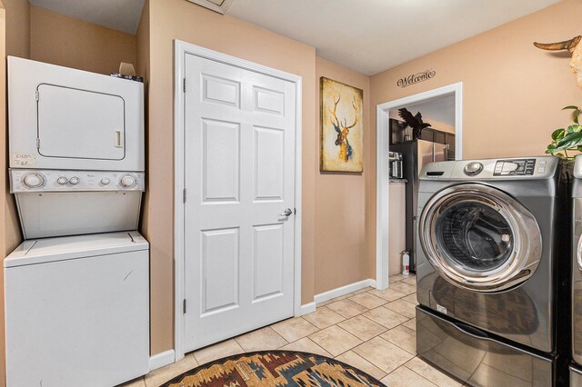 clothes washing area featuring light tile patterned floors and stacked washer and dryer