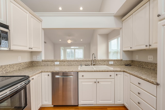 kitchen with light stone counters, stainless steel appliances, vaulted ceiling, ceiling fan, and sink