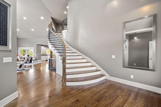 stairs featuring recessed lighting, a high ceiling, wood finished floors, visible vents, and baseboards