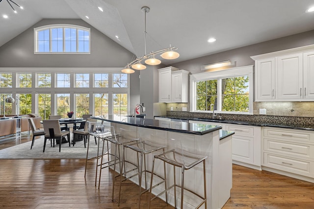 kitchen with white cabinets, dark countertops, wood finished floors, a kitchen bar, and a sink