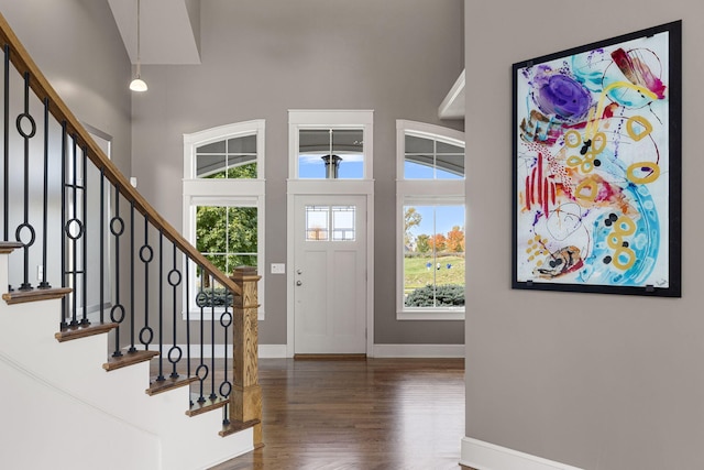 entrance foyer with stairs, wood finished floors, a towering ceiling, and baseboards