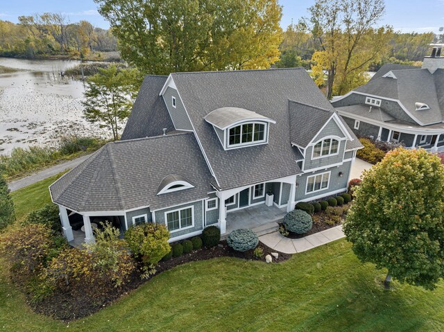 exterior space with a shingled roof, a water view, and a lawn