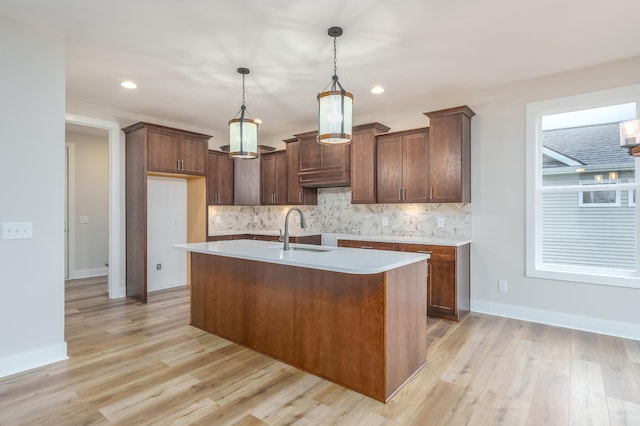 kitchen featuring sink, hanging light fixtures, light hardwood / wood-style flooring, an island with sink, and decorative backsplash