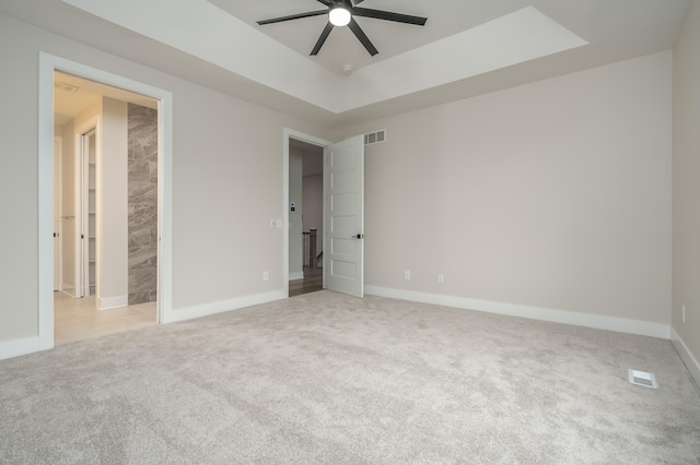 unfurnished bedroom featuring light carpet, a tray ceiling, and ceiling fan