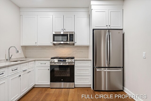 kitchen featuring white cabinets, sink, light hardwood / wood-style flooring, light stone countertops, and stainless steel appliances