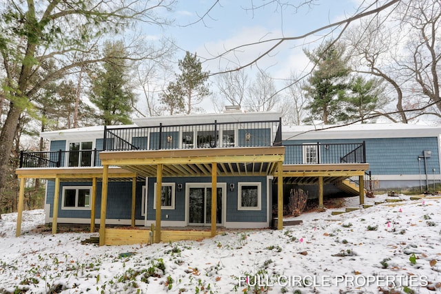 snow covered back of property with a wooden deck