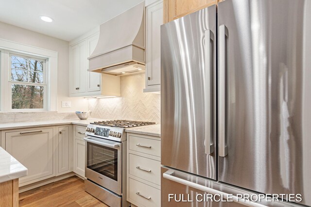 kitchen featuring decorative backsplash, custom range hood, stainless steel appliances, and light hardwood / wood-style floors