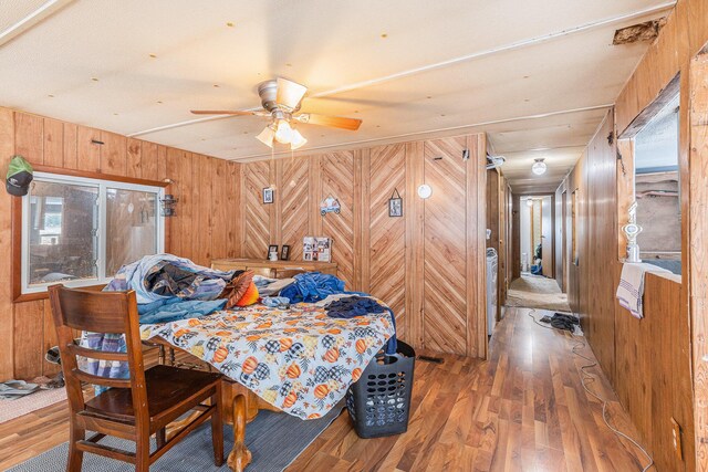 bedroom with hardwood / wood-style flooring, ceiling fan, and wood walls