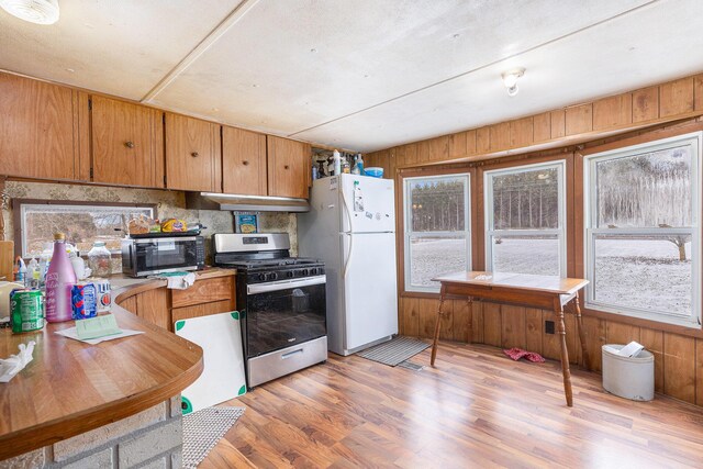 kitchen featuring decorative backsplash, wood walls, appliances with stainless steel finishes, and light hardwood / wood-style flooring