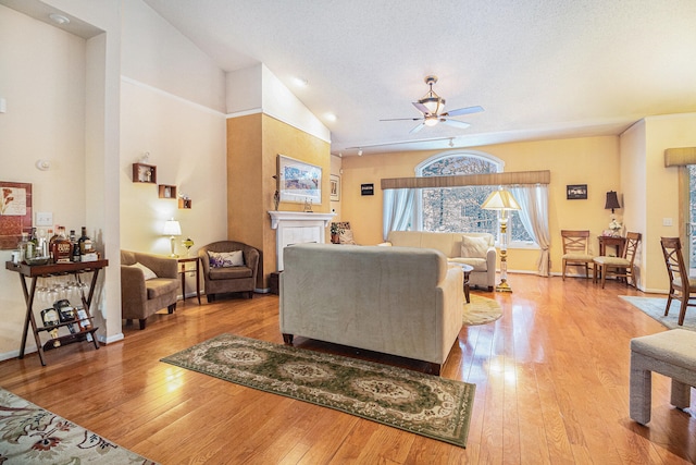 living room with a textured ceiling, ceiling fan, light hardwood / wood-style floors, and vaulted ceiling