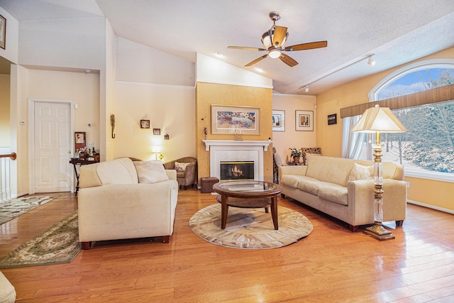 living room featuring light wood-type flooring, a textured ceiling, ceiling fan, a fireplace, and lofted ceiling