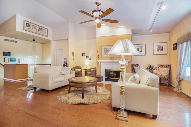 living room with ceiling fan with notable chandelier, light wood-type flooring, and lofted ceiling