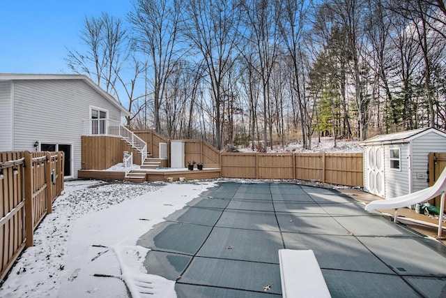 snow covered pool featuring a diving board, a wooden deck, a storage shed, and a water slide