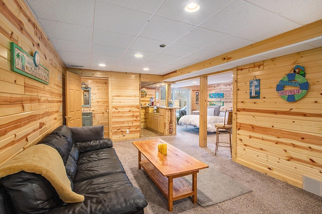 living room featuring a paneled ceiling, wooden walls, and carpet floors