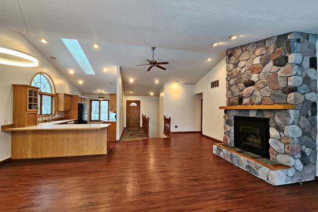 kitchen featuring black refrigerator, a skylight, dark hardwood / wood-style floors, a fireplace, and kitchen peninsula