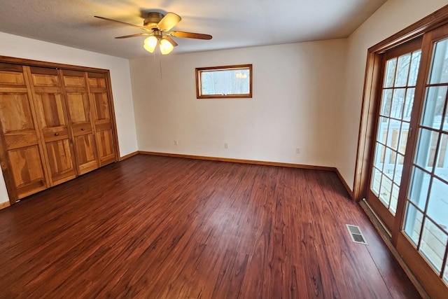 unfurnished bedroom with ceiling fan, a closet, dark wood-type flooring, and multiple windows