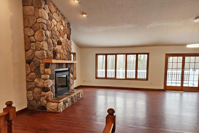 unfurnished living room with vaulted ceiling, a textured ceiling, a stone fireplace, wood finished floors, and baseboards