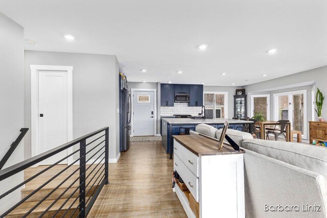 kitchen with blue cabinets, light wood-type flooring, appliances with stainless steel finishes, tasteful backsplash, and white cabinetry