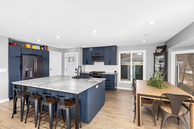 kitchen with blue cabinetry, sink, decorative backsplash, appliances with stainless steel finishes, and light wood-type flooring