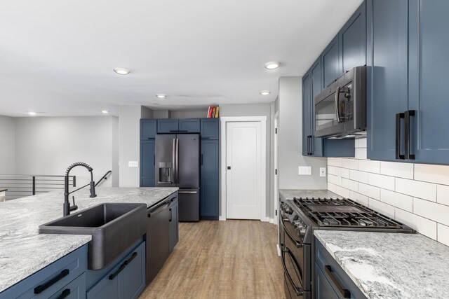 kitchen with sink, stainless steel appliances, tasteful backsplash, blue cabinets, and light wood-type flooring