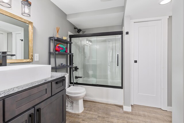 full bathroom with hardwood / wood-style flooring, vanity, toilet, and shower / bath combination with glass door