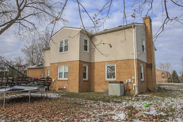 snow covered back of property with central AC unit and a trampoline