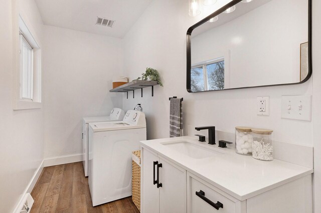 laundry area with hardwood / wood-style flooring, washing machine and dryer, sink, and a wealth of natural light