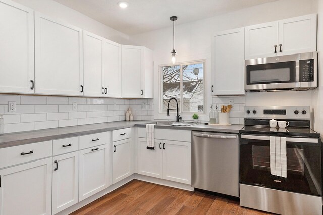 kitchen with white cabinetry, backsplash, light hardwood / wood-style floors, decorative light fixtures, and appliances with stainless steel finishes