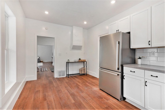 kitchen featuring white cabinets, decorative backsplash, light hardwood / wood-style flooring, and stainless steel refrigerator