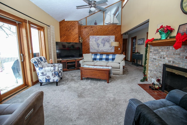 carpeted living room with ceiling fan, high vaulted ceiling, wood walls, and a brick fireplace