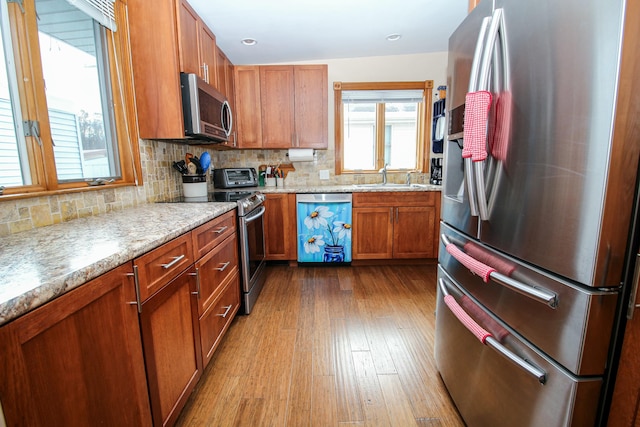 kitchen with backsplash, sink, light stone countertops, light wood-type flooring, and appliances with stainless steel finishes