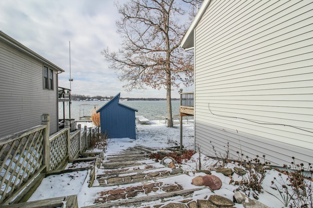 snowy yard featuring a water view and a storage unit