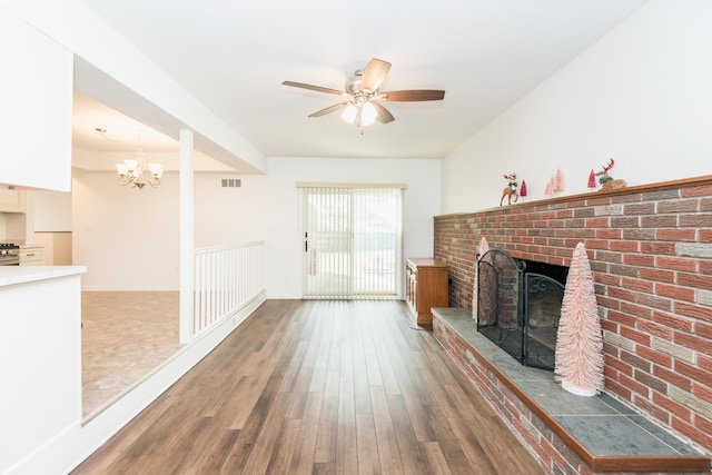 unfurnished living room with ceiling fan with notable chandelier, dark hardwood / wood-style flooring, and a brick fireplace