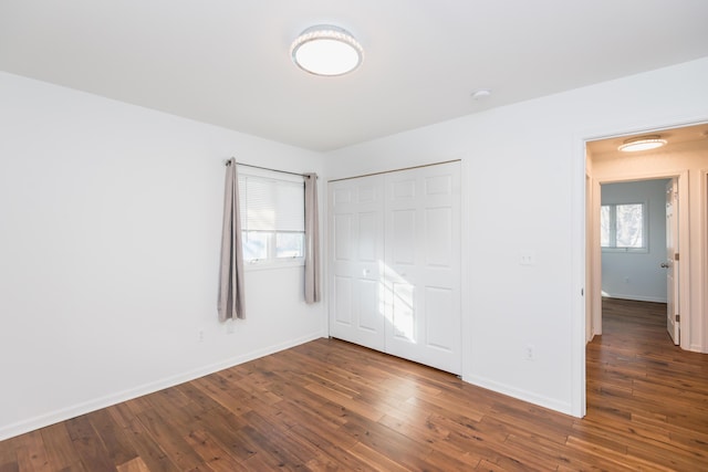 unfurnished bedroom featuring multiple windows, a closet, and dark wood-type flooring