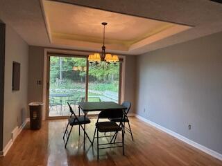 dining space with hardwood / wood-style flooring, a raised ceiling, and a notable chandelier